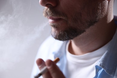 Photo of Man smoking cigarette on light background, closeup