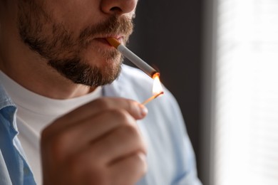 Photo of Man lighting cigarette with match on blurred background, closeup