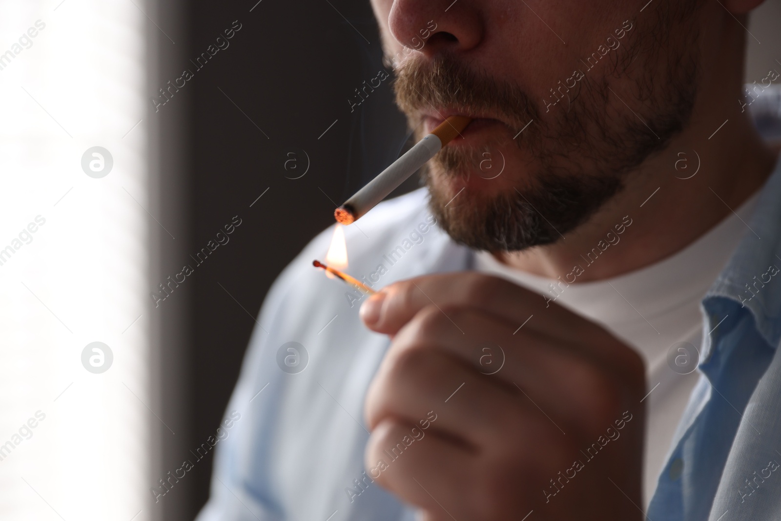 Man lighting cigarette with match on blurred background, closeup Photo of Man lighting cigarette with match on blurred background, closeup