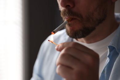 Photo of Man lighting cigarette with match on blurred background, closeup