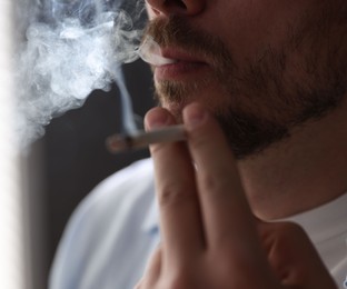Photo of Man smoking cigarette on blurred background, closeup
