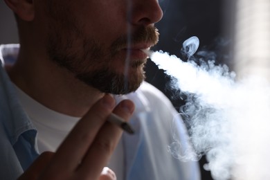 Photo of Man smoking cigarette on blurred background, closeup