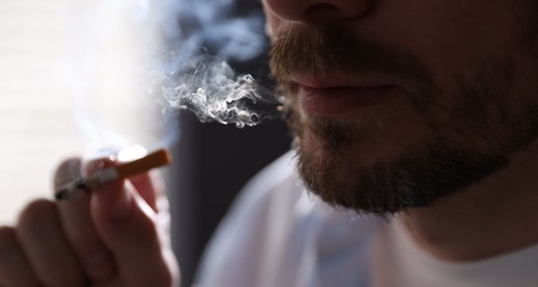 Photo of Man smoking cigarette on blurred background, closeup