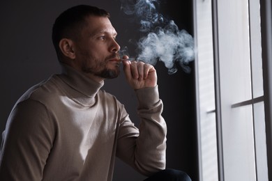 Photo of Man smoking cigarette near window in room