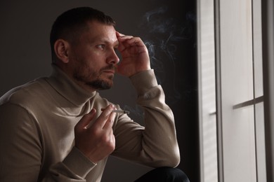 Photo of Man smoking cigarette near window in room