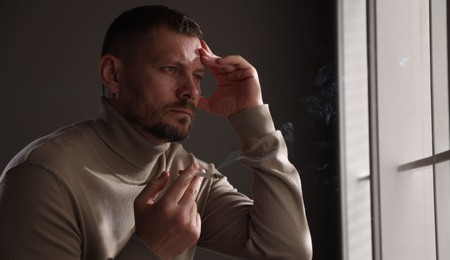 Photo of Man smoking cigarette near window in room