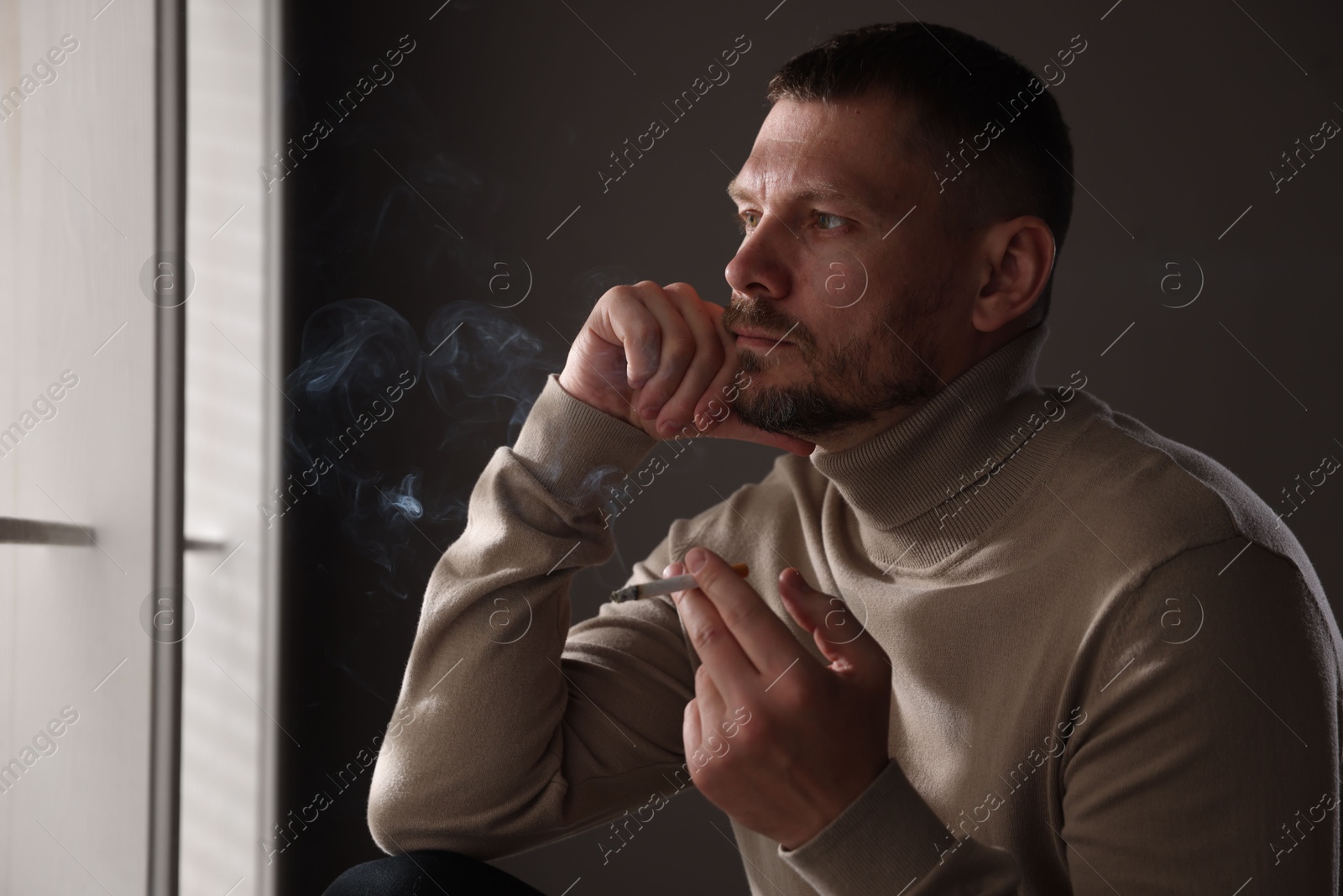 Man smoking cigarette near window in room Photo of Man smoking cigarette near window in room