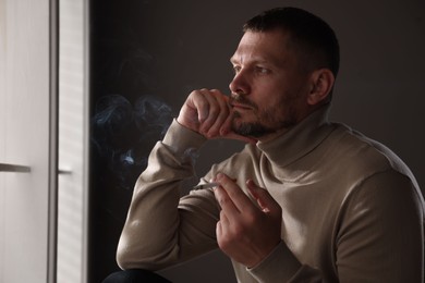 Photo of Man smoking cigarette near window in room