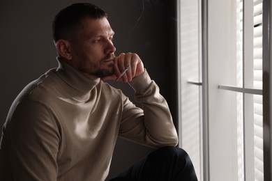 Photo of Man smoking cigarette near window in room