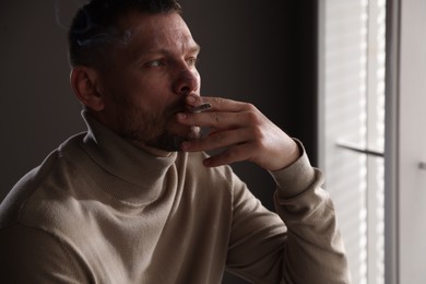 Photo of Man smoking cigarette near window in room