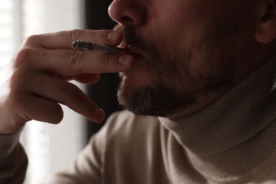 Photo of Man smoking cigarette near window indoors, closeup