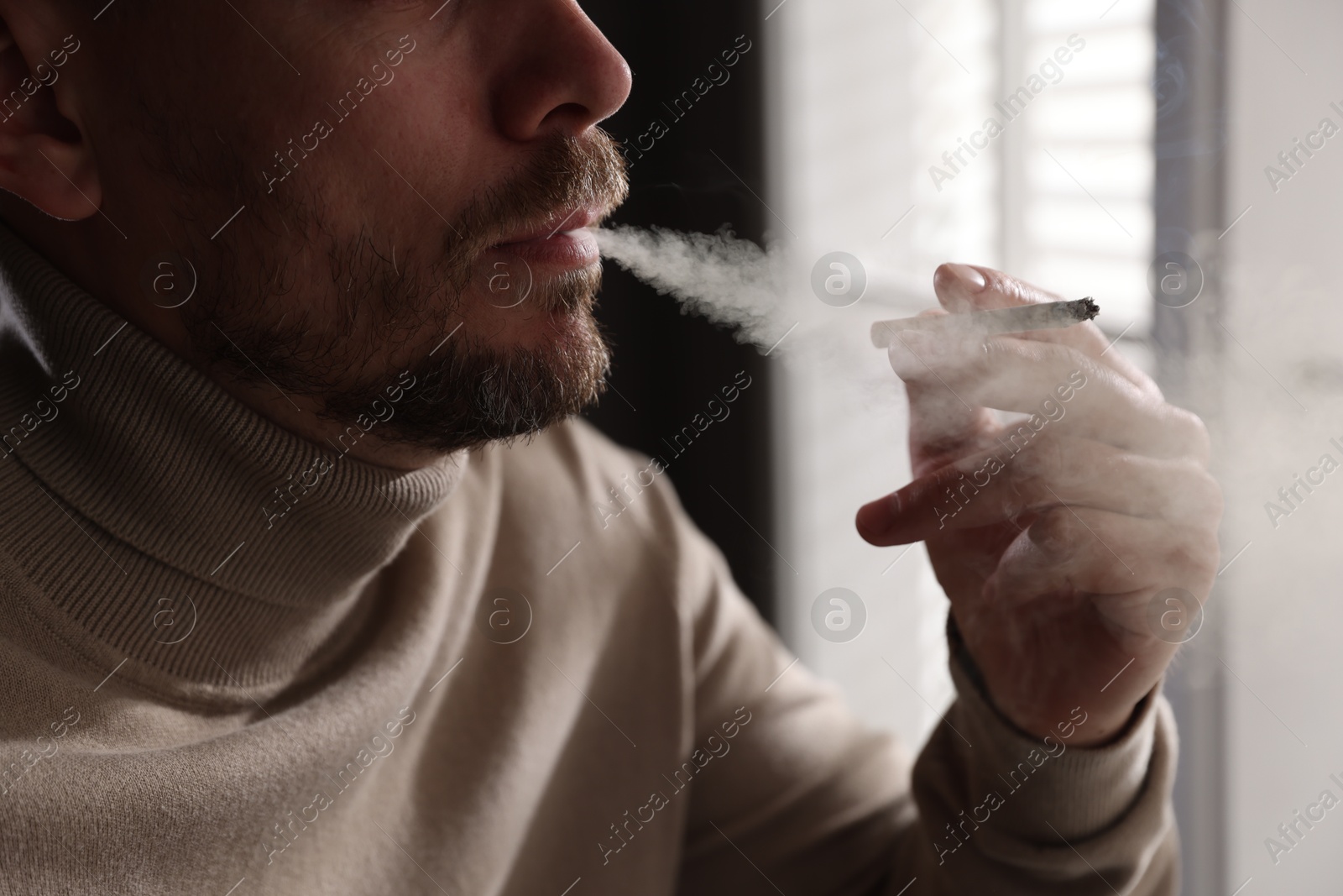 Man smoking cigarette near window indoors, closeup Photo of Man smoking cigarette near window indoors, closeup