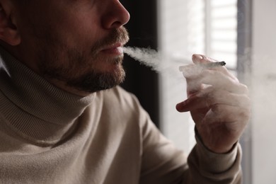 Photo of Man smoking cigarette near window indoors, closeup