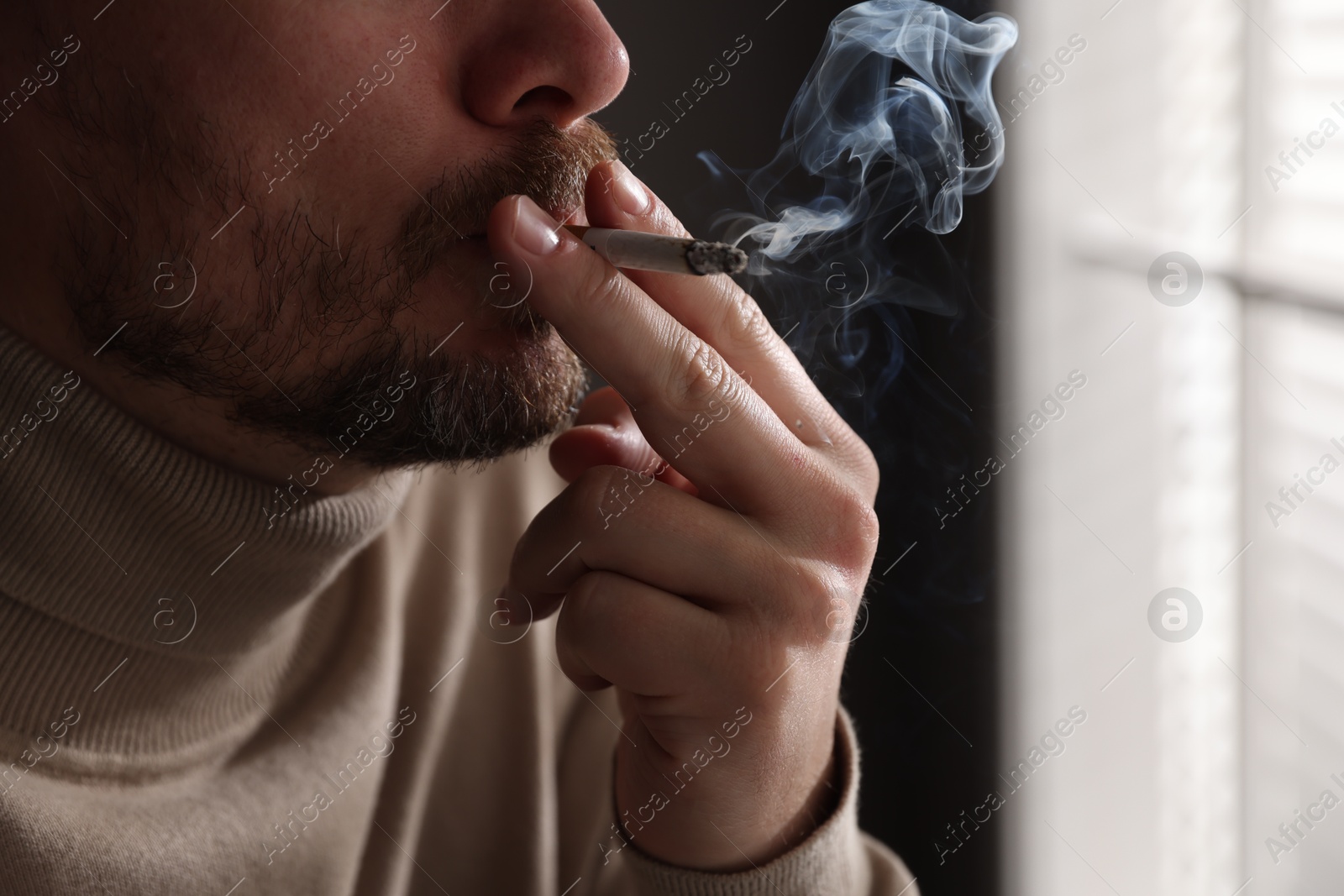 Man smoking cigarette near window indoors, closeup Photo of Man smoking cigarette near window indoors, closeup