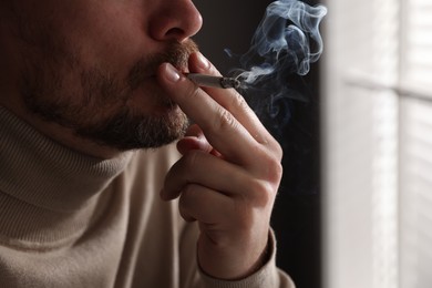 Photo of Man smoking cigarette near window indoors, closeup