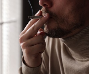 Photo of Man smoking cigarette near window indoors, closeup