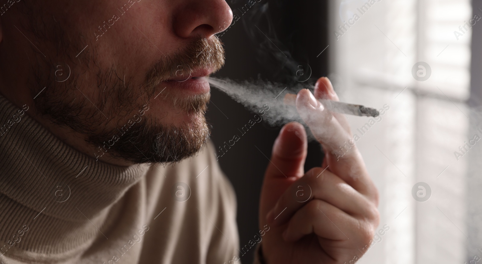 Man smoking cigarette near window indoors, closeup Photo of Man smoking cigarette near window indoors, closeup