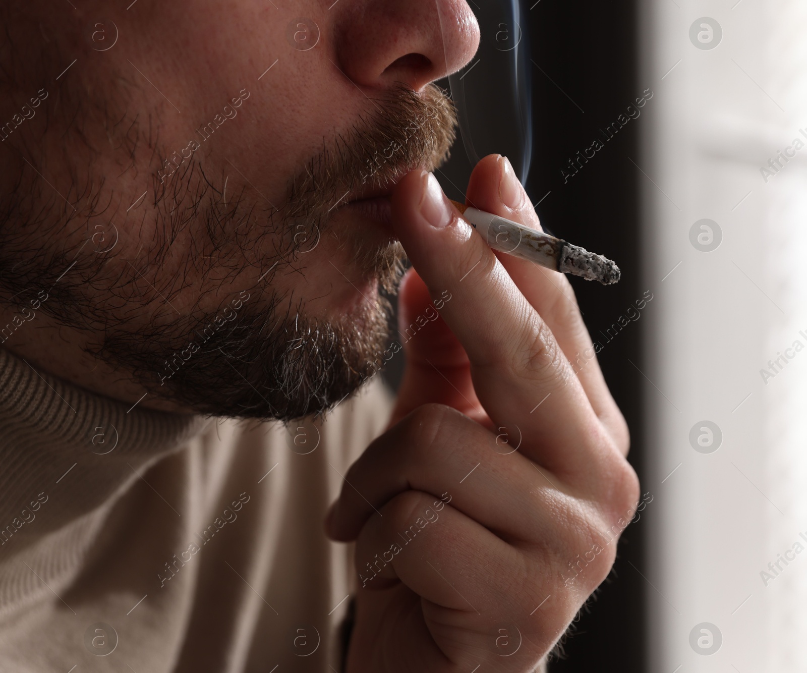 Man smoking cigarette near window indoors, closeup Photo of Man smoking cigarette near window indoors, closeup
