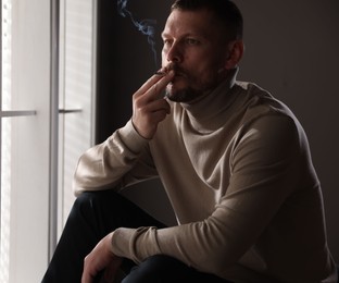 Photo of Man smoking cigarette near window in room
