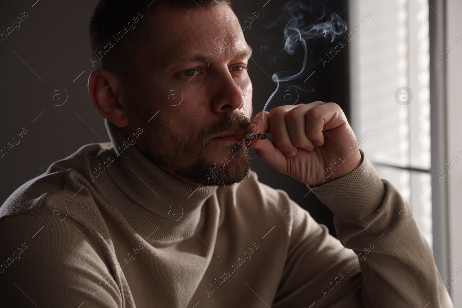 Man smoking cigarette near window in room Photo of Man smoking cigarette near window in room
