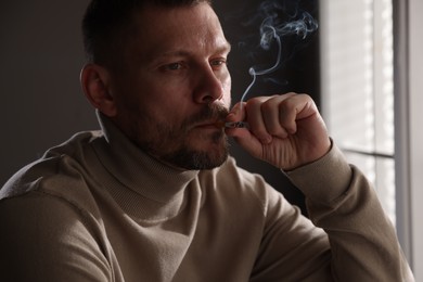 Photo of Man smoking cigarette near window in room