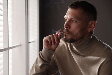 Photo of Man smoking cigarette near window in room