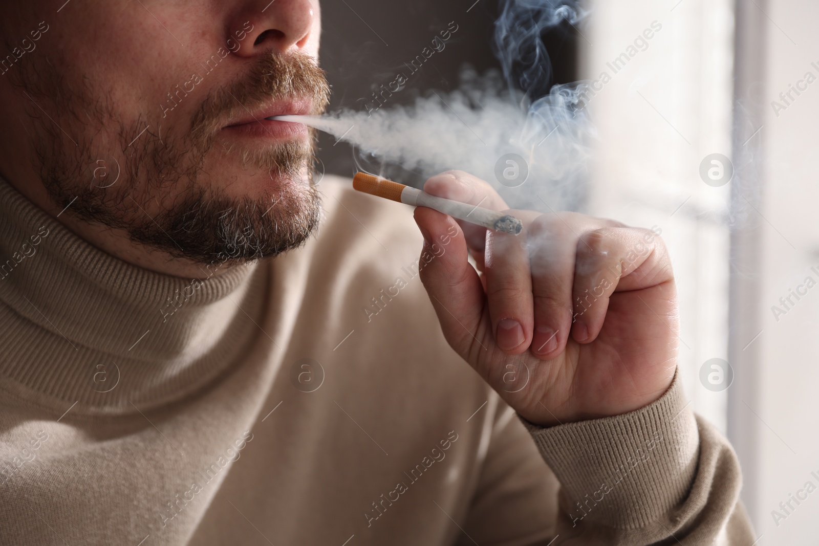 Man smoking cigarette near window indoors, closeup Photo of Man smoking cigarette near window indoors, closeup