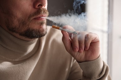 Photo of Man smoking cigarette near window indoors, closeup