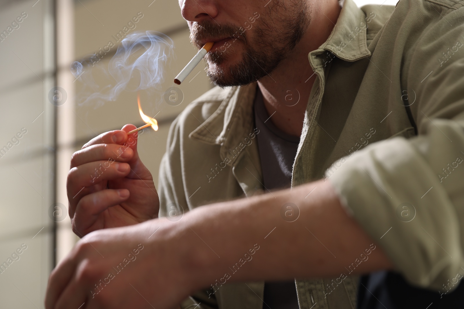 Man lighting cigarette with match on blurred background, closeup Photo of Man lighting cigarette with match on blurred background, closeup