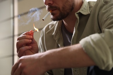 Photo of Man lighting cigarette with match on blurred background, closeup