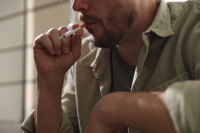 Photo of Man smoking cigarette on blurred background, closeup