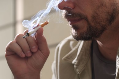 Photo of Man smoking cigarette on blurred background, closeup