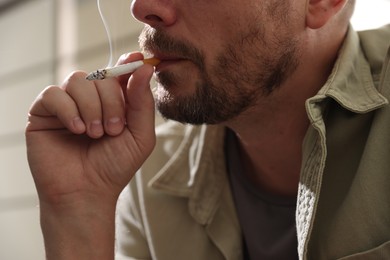 Photo of Man smoking cigarette on blurred background, closeup