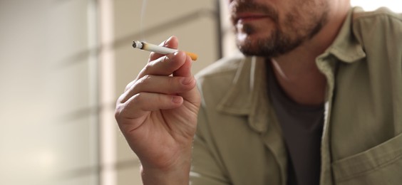 Photo of Man smoking cigarette on blurred background, closeup. Space for text