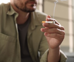 Photo of Man smoking cigarette on blurred background, closeup