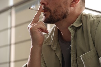 Photo of Man smoking cigarette on blurred background, closeup