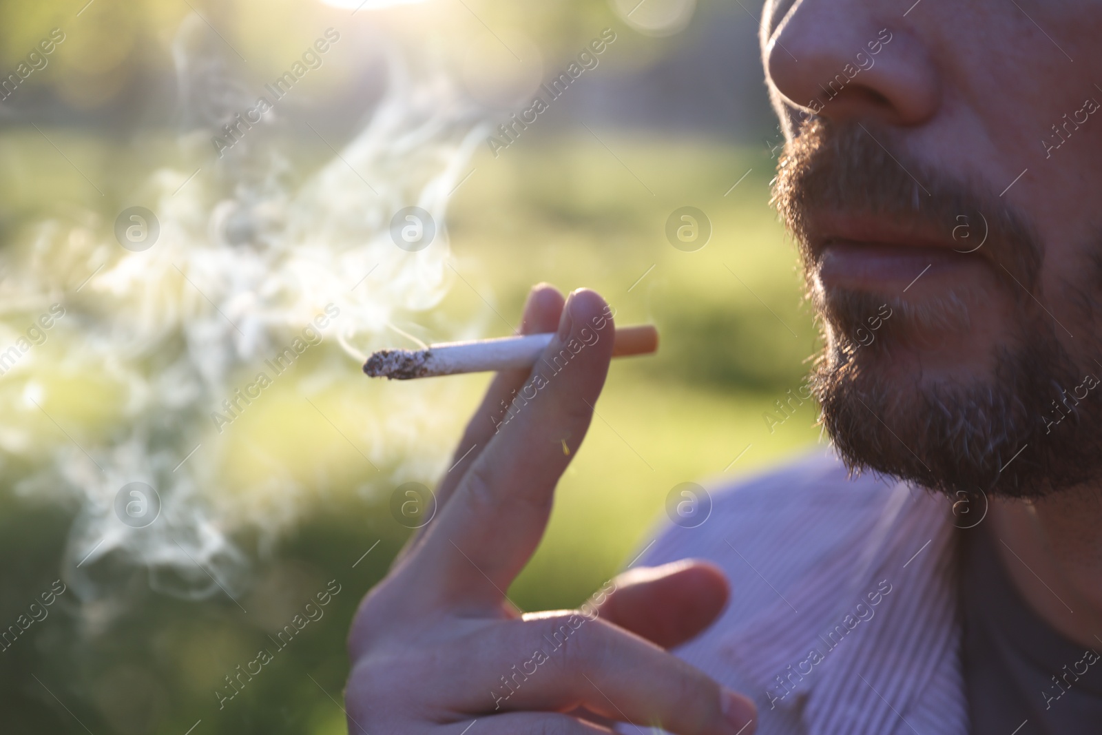 Man smoking cigarette outdoors on sunny day, closeup Photo of Man smoking cigarette outdoors on sunny day, closeup