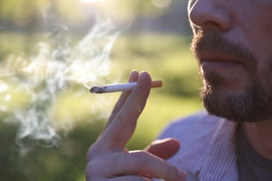 Photo of Man smoking cigarette outdoors on sunny day, closeup