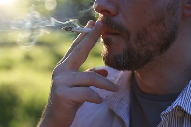 Photo of Man smoking cigarette on blurred background, closeup