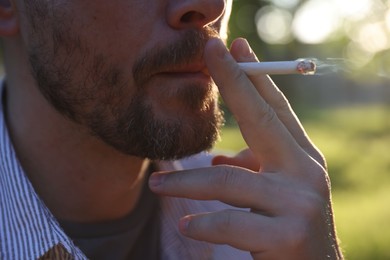 Photo of Man smoking cigarette on blurred background, closeup