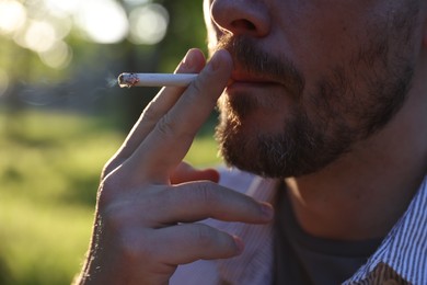 Photo of Man smoking cigarette on blurred background, closeup