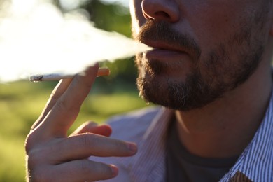 Photo of Man smoking cigarette on blurred background, closeup