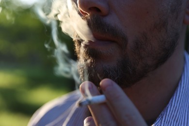 Photo of Man smoking cigarette on blurred background, closeup