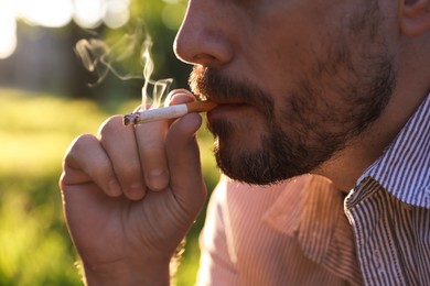 Photo of Man smoking cigarette on blurred background, closeup