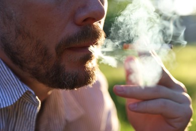 Photo of Man smoking cigarette on blurred background, closeup