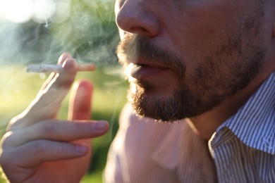 Photo of Man smoking cigarette on blurred background, closeup