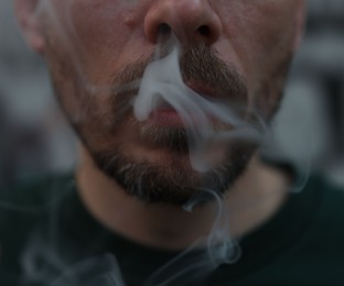 Photo of Man smoking cigarette on blurred background, closeup