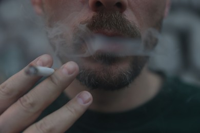Photo of Man smoking cigarette on blurred background, closeup