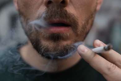 Photo of Man smoking cigarette on blurred background, closeup