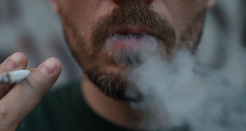 Photo of Man smoking cigarette on blurred background, closeup